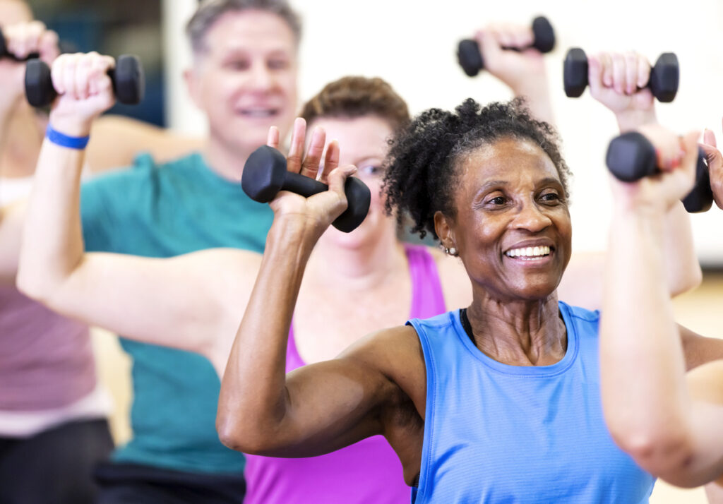 Senior African-American woman in exercise class smiling while lifting hand weights.