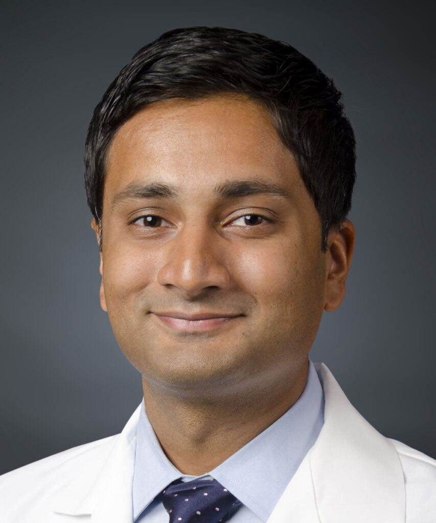Dr. Rahman smiling with labcoat and tie on.