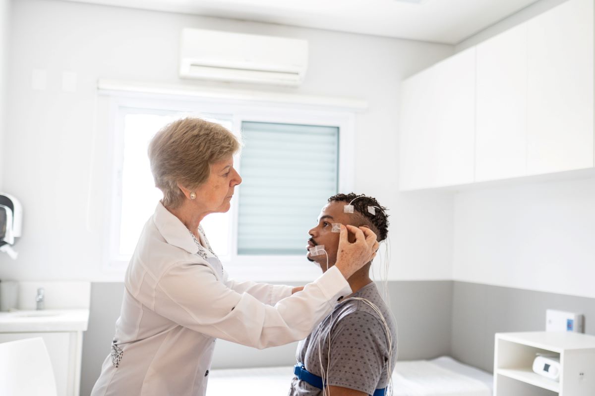 A doctor places sensors on a patient's head in preparation for a sleep study.