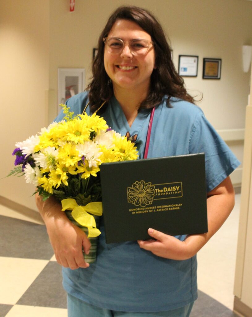 Candace in scrubs holding bouquet of Daisies.