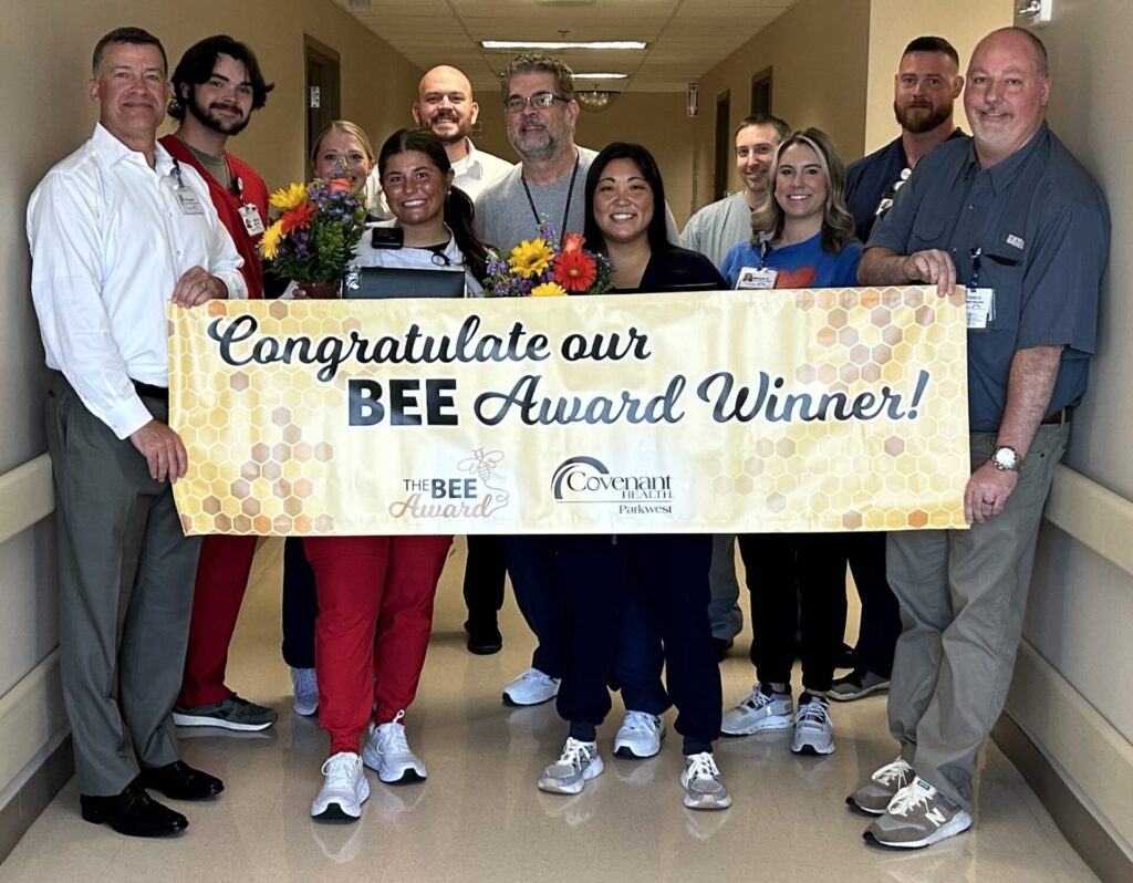 Laci pictured in the hallway with flowers with co-workers and members of leadership holding BEE banner. 