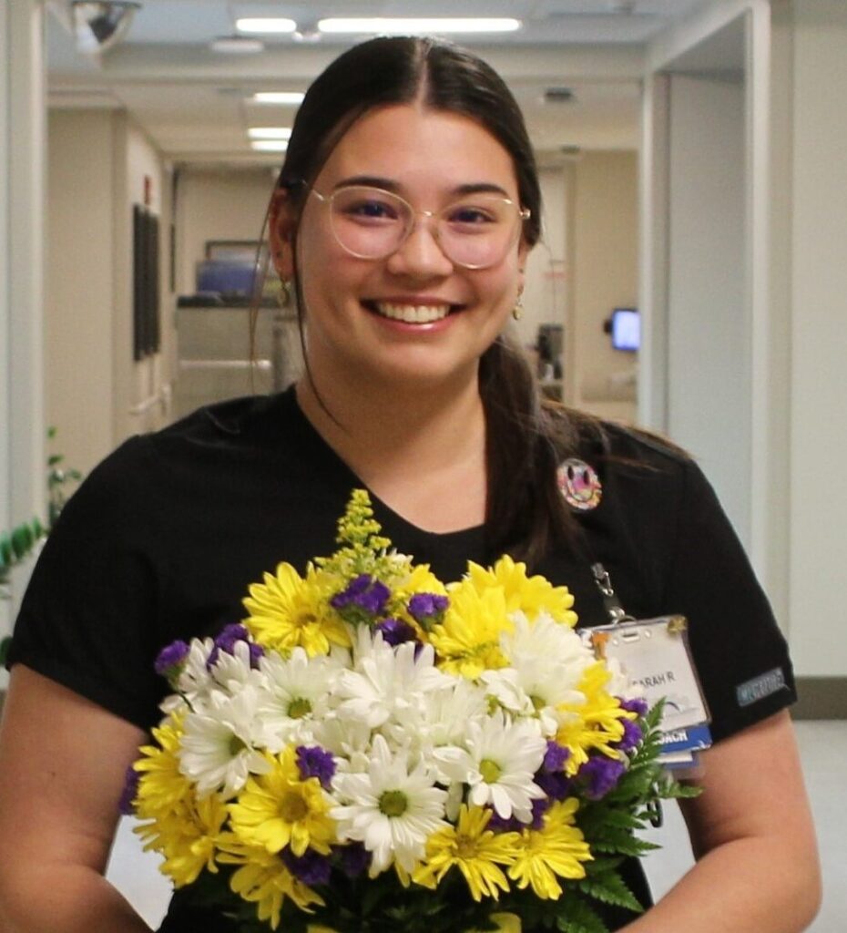 Nurse in black scrubs holding daisies