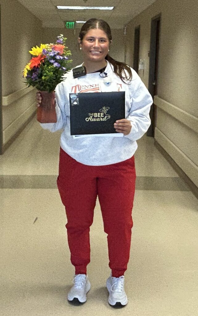 Maddie standing in hallway smiling with her flower bouquet and BEE certificate.