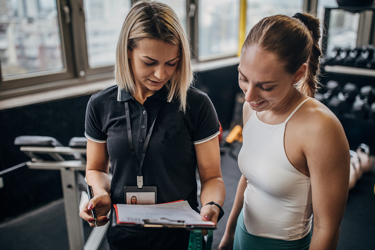 Young woman talking with her female personal trainer about her progress in the gym.