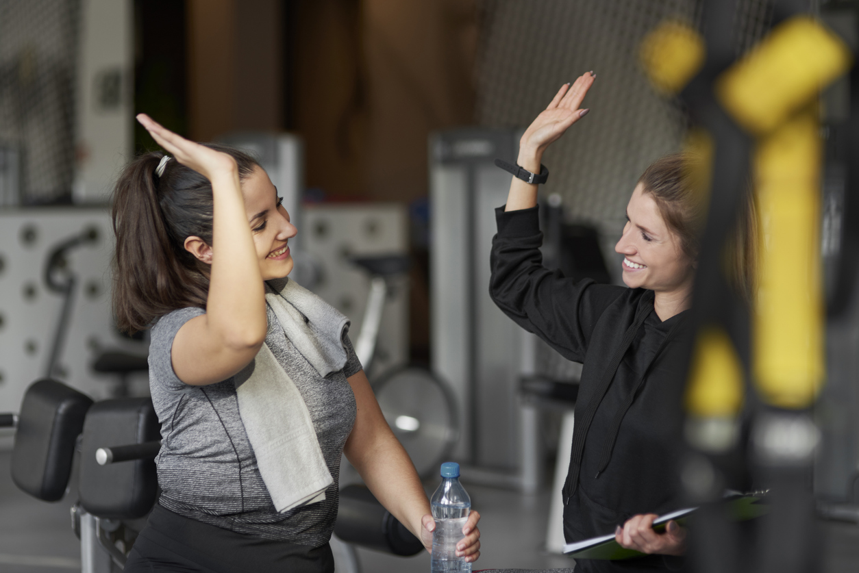 A female fitness instructor high-fives her client during a personal training session at the gym.