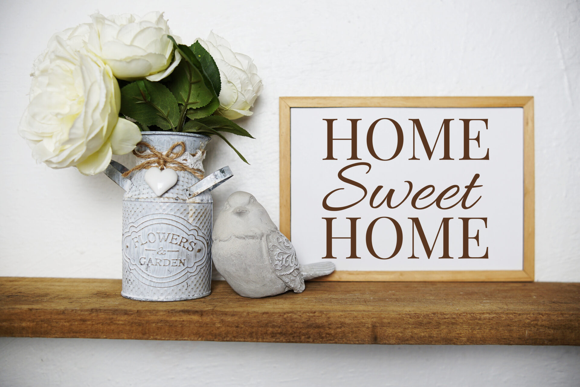 Home Sweet Home sign on wooden shelf next to vase of white flowers and ceramic bird