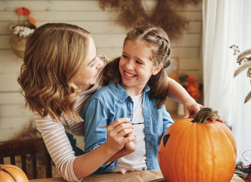 Woman and female childe decorate a pumpkin with paints as a Halloween safety alterntive to carving.