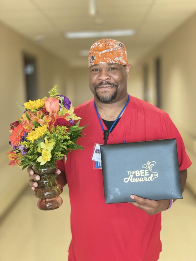 African american male smiling holding certificate and flowers.