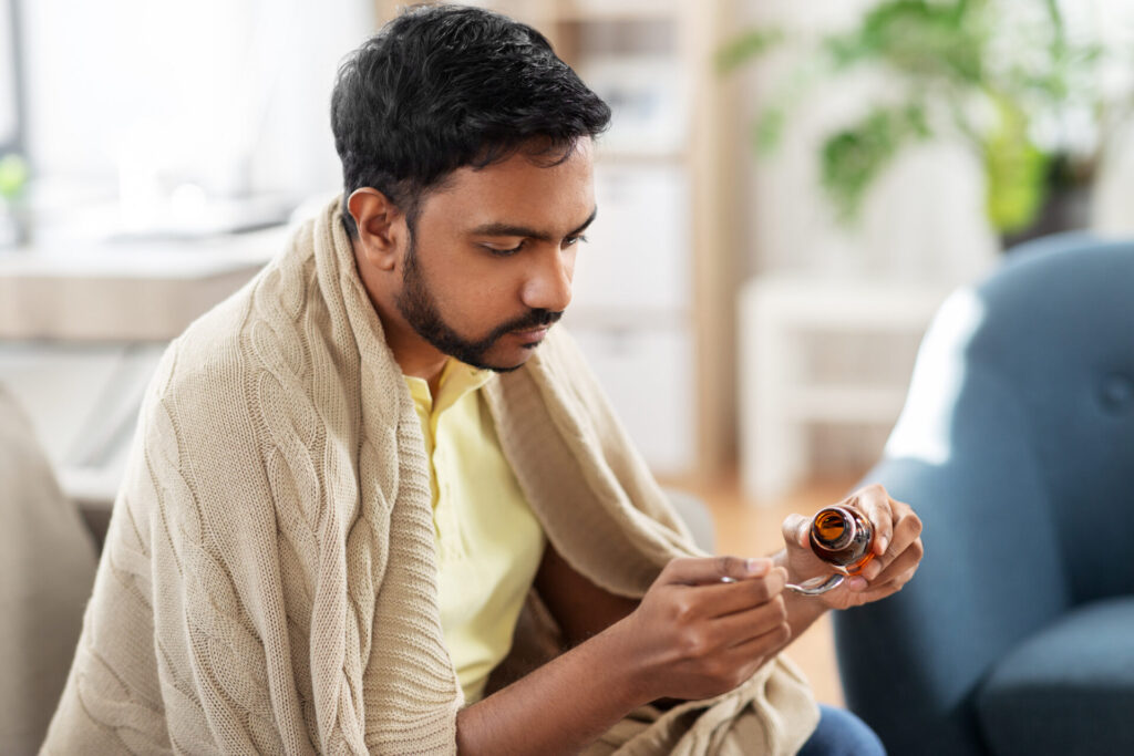 Man wrapped in blanket pours cough medicine into a spoon