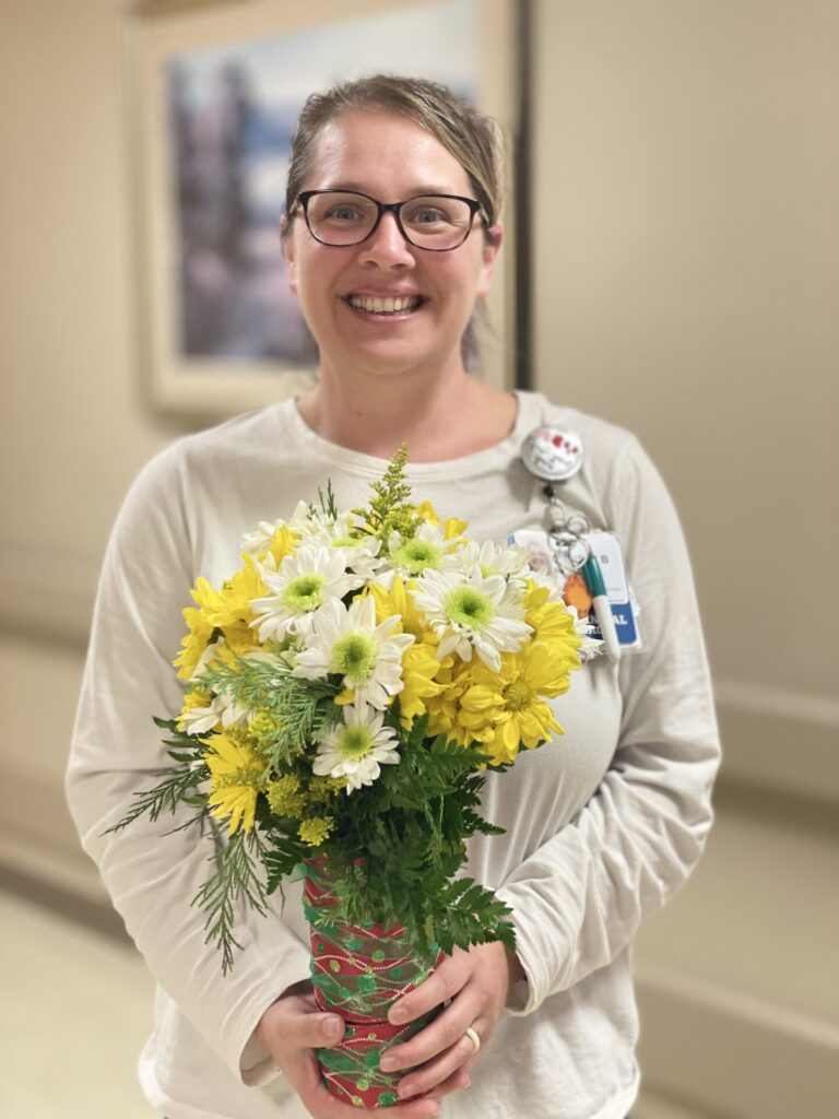 Christy smiling holding arrangement of daisies.