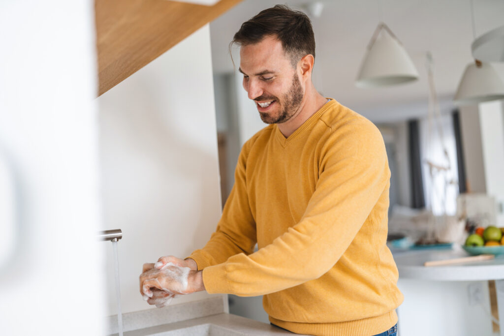 Dark-haired man washing hands to prevent illnesses like sore throat