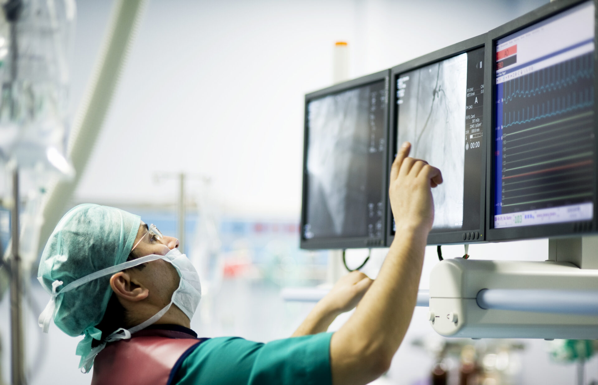 A cardiologist doctor examines images on multiple computer screens in an operating room.