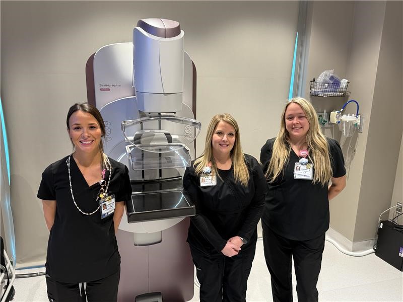 Three female staff members in black scrubs standing near new biopsy machine at LeConte Comprehensive Breast Center