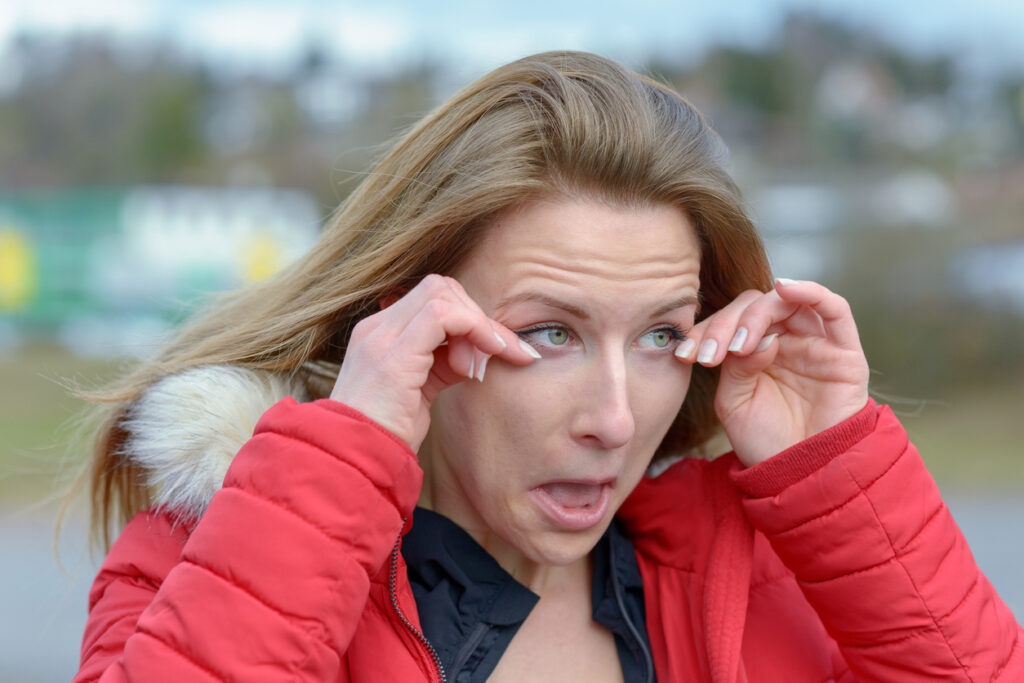 Woman wearing red coat outdoors rubbing eyes because of winter allergies