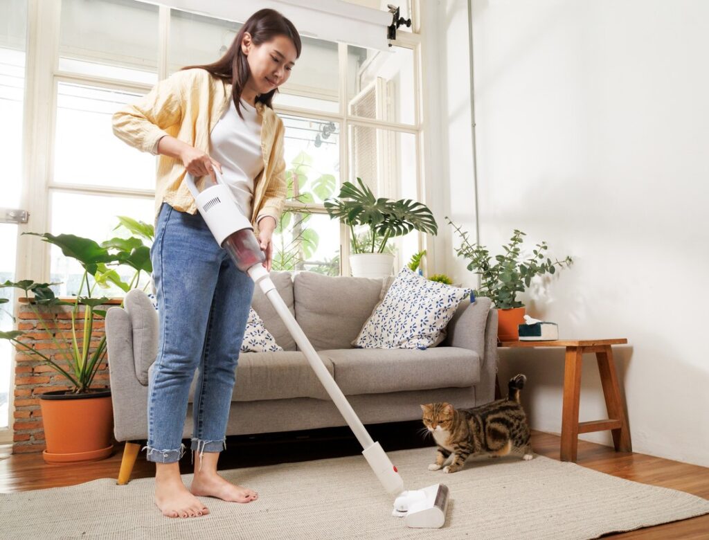 Woman running vacuum indoors with cat nearby Vacuuming often helps with winter allergies.