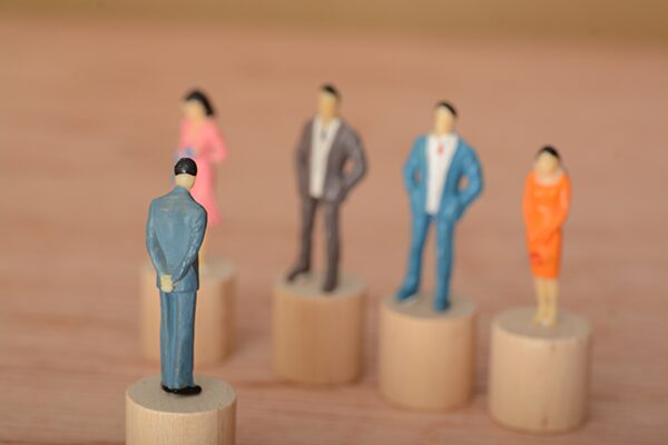 Toy figurine business men and women stand across from their manager who is looking down on them.