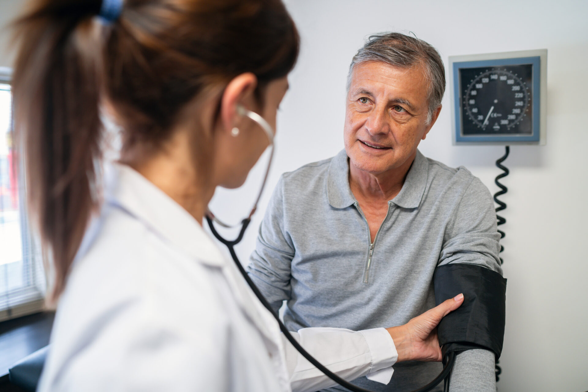 Senior male patient having his blood pressure measured by a female healthcare professional in a medical office setting.