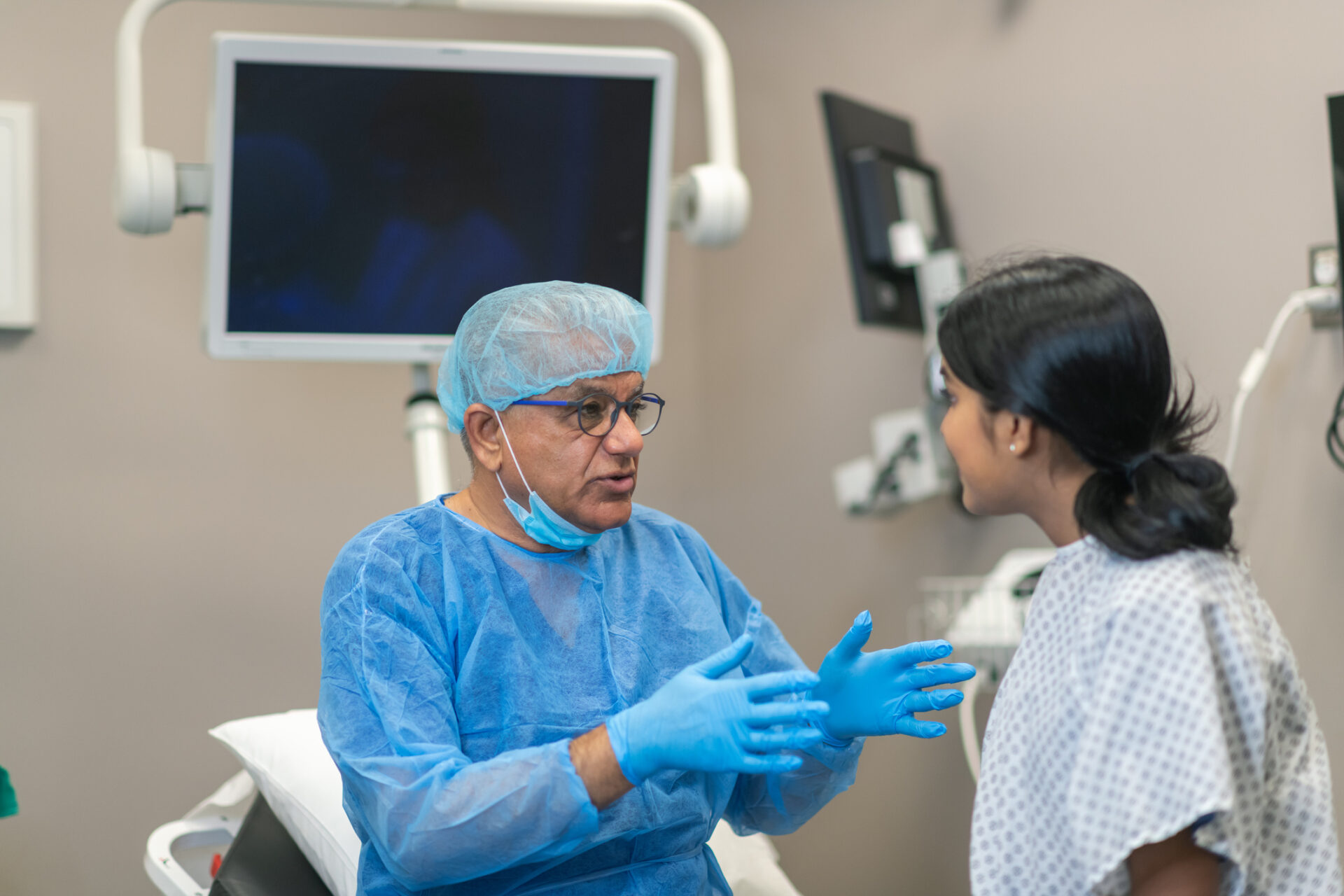 A male surgeon meets with a female patient in a hospital operating room to explain what will be done during surgery.